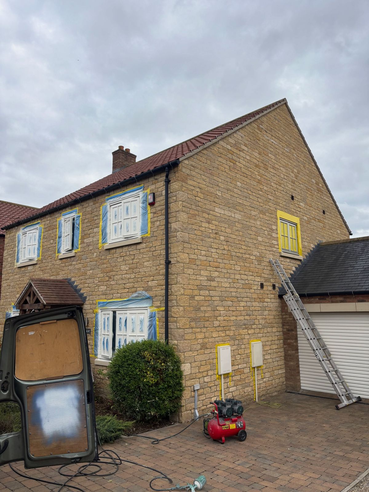 Stone house side elevation with windows masked and spray kit set up on the drive